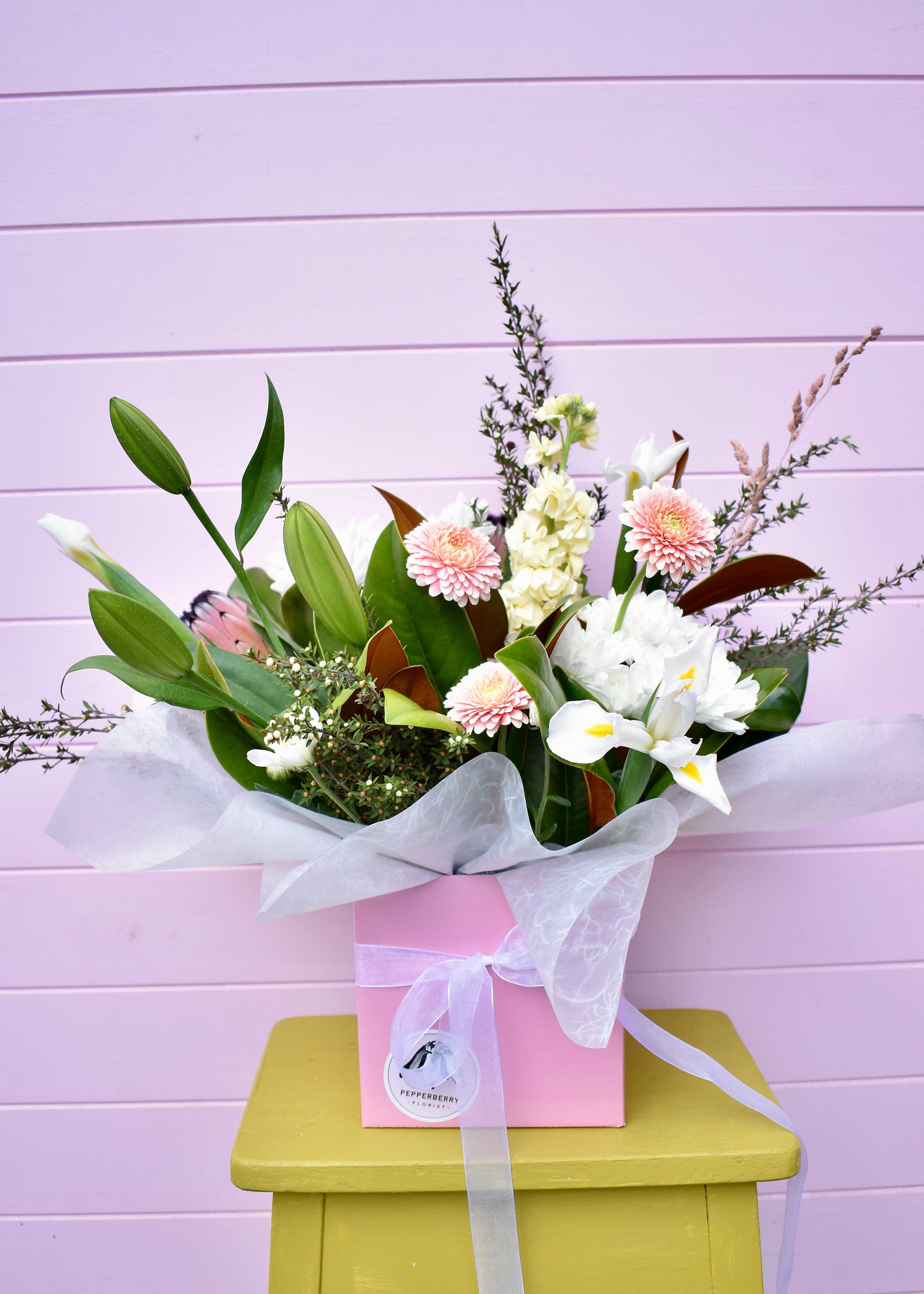 Bouquet of flowers in a pink box on a green stool against a light purple wall