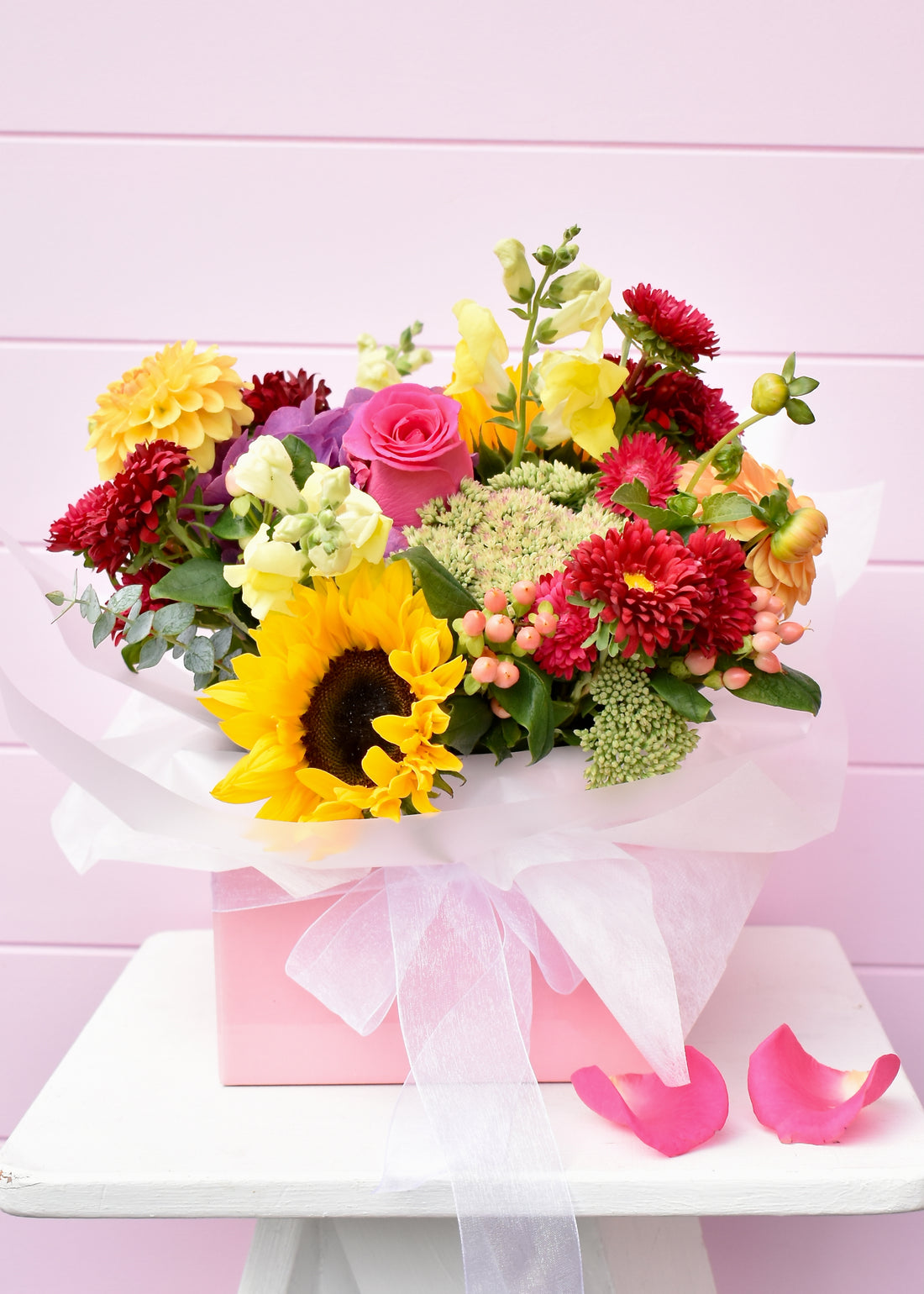Bright coloured flowers in a pink box. Includes sunflowers, pink roses and daisies