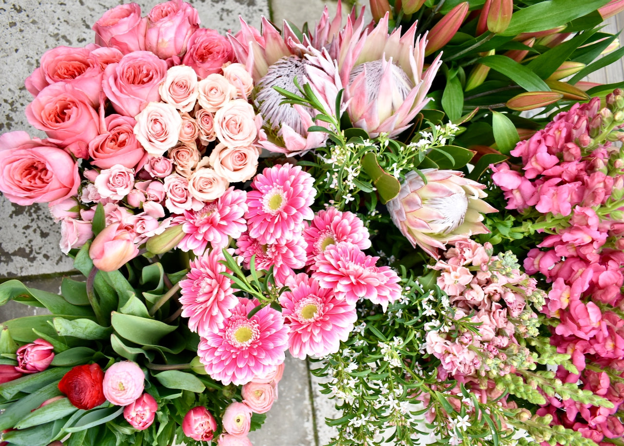 Top view of lots of pink fresh flowers. Snap dragons, tulips, rose, protea, gerbera in various shades of pink