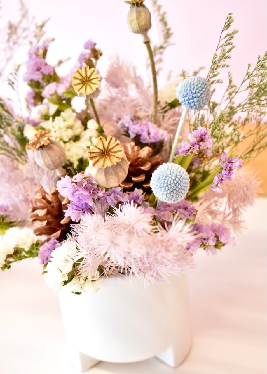 Pretty dried flower arrangement in a small white ceramic pot. Colours of pale blue, mauve and white.