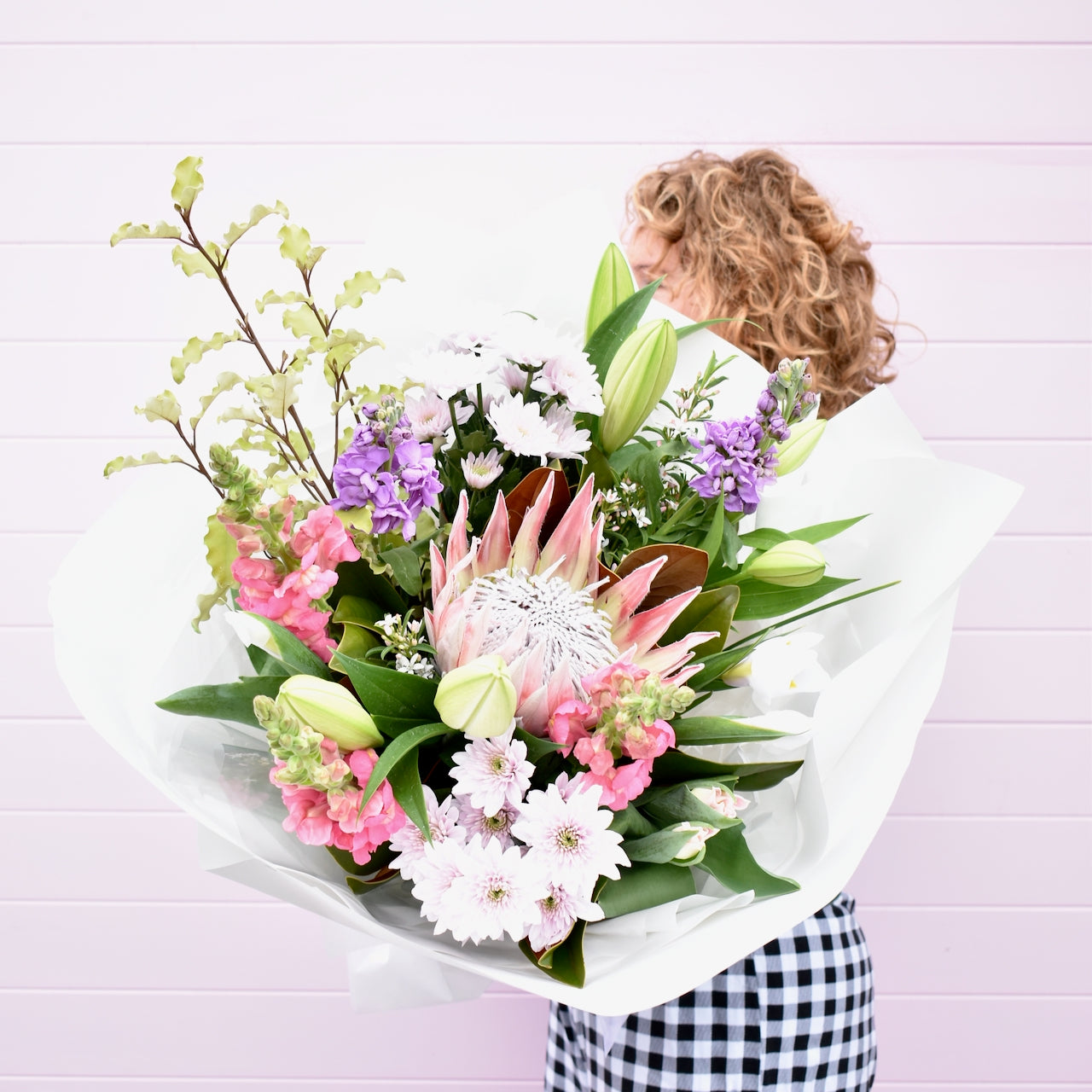 Large flower bouquet, held by florist. White, purple and pink with proteas and lilies