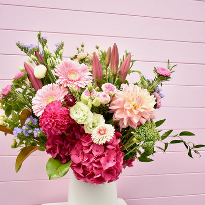 A large and beautiful flower arrangement in a white vase with large pink flowers