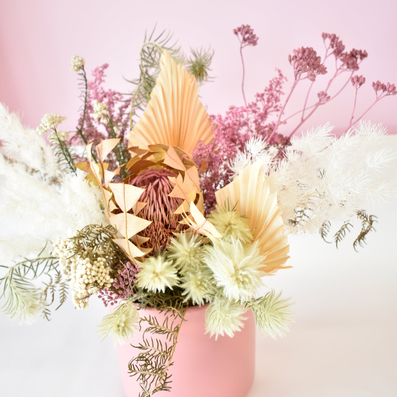 Dried flower arrangement in a pink ceramic pot. Colours of cream, white, peach and pink, designed by florist