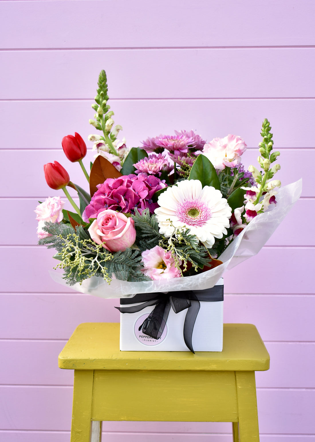 White box containing a fresh flower arrangement in pink, purple, red &amp; blue