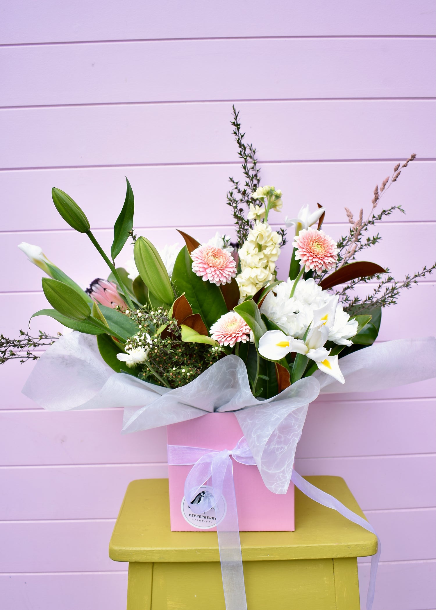 Bouquet of flowers in a pink box on a green stool against a light purple wall