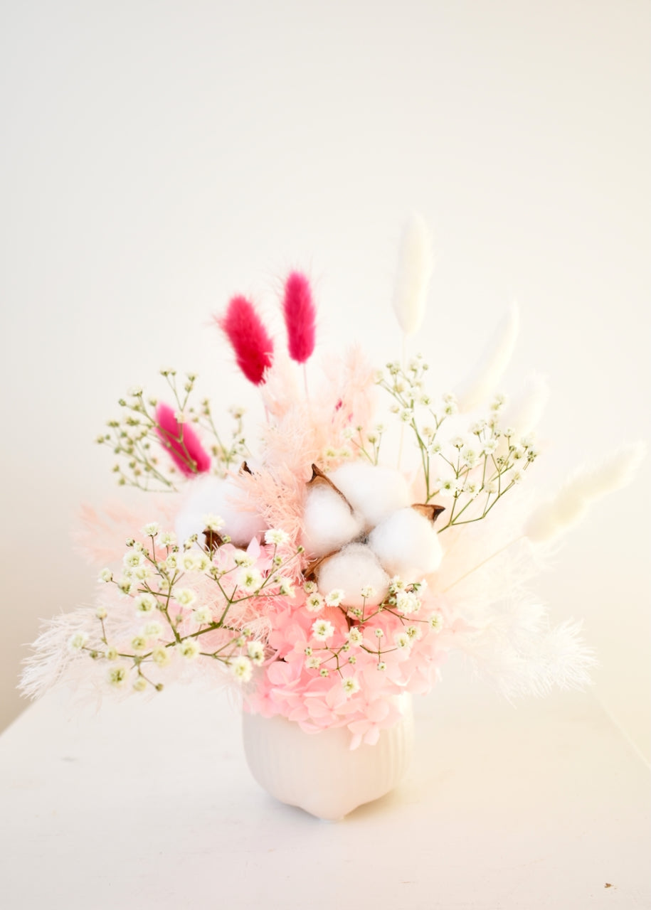 Small white and pink dried flower arrangement in white pot. Created with cotton flowers, hydrangea, gypsophlia and bunny tails in white, pale pink and hot pink