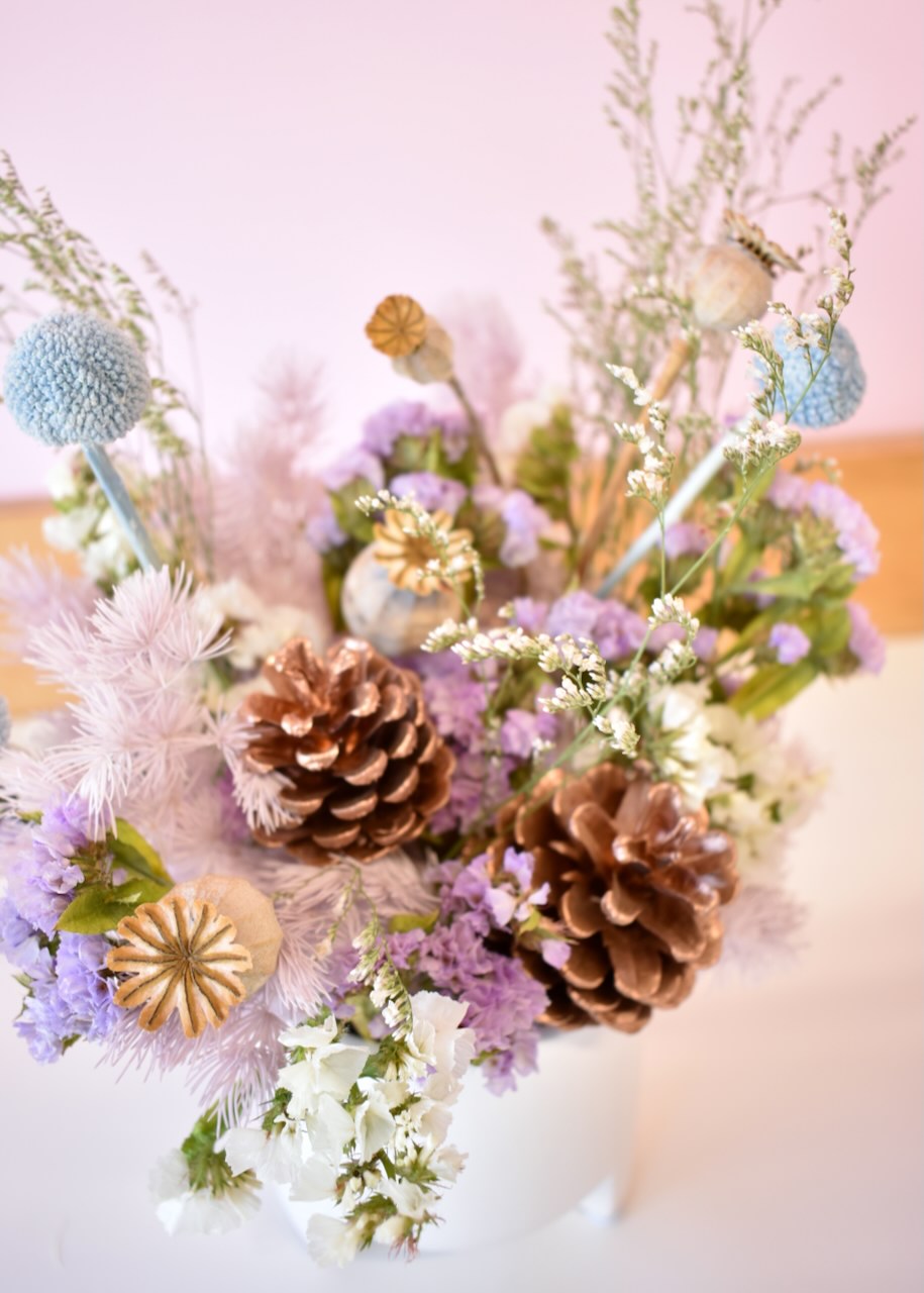 Pretty dried flower arrangement in a small white ceramic pot. Colours of pale blue, mauve and white.