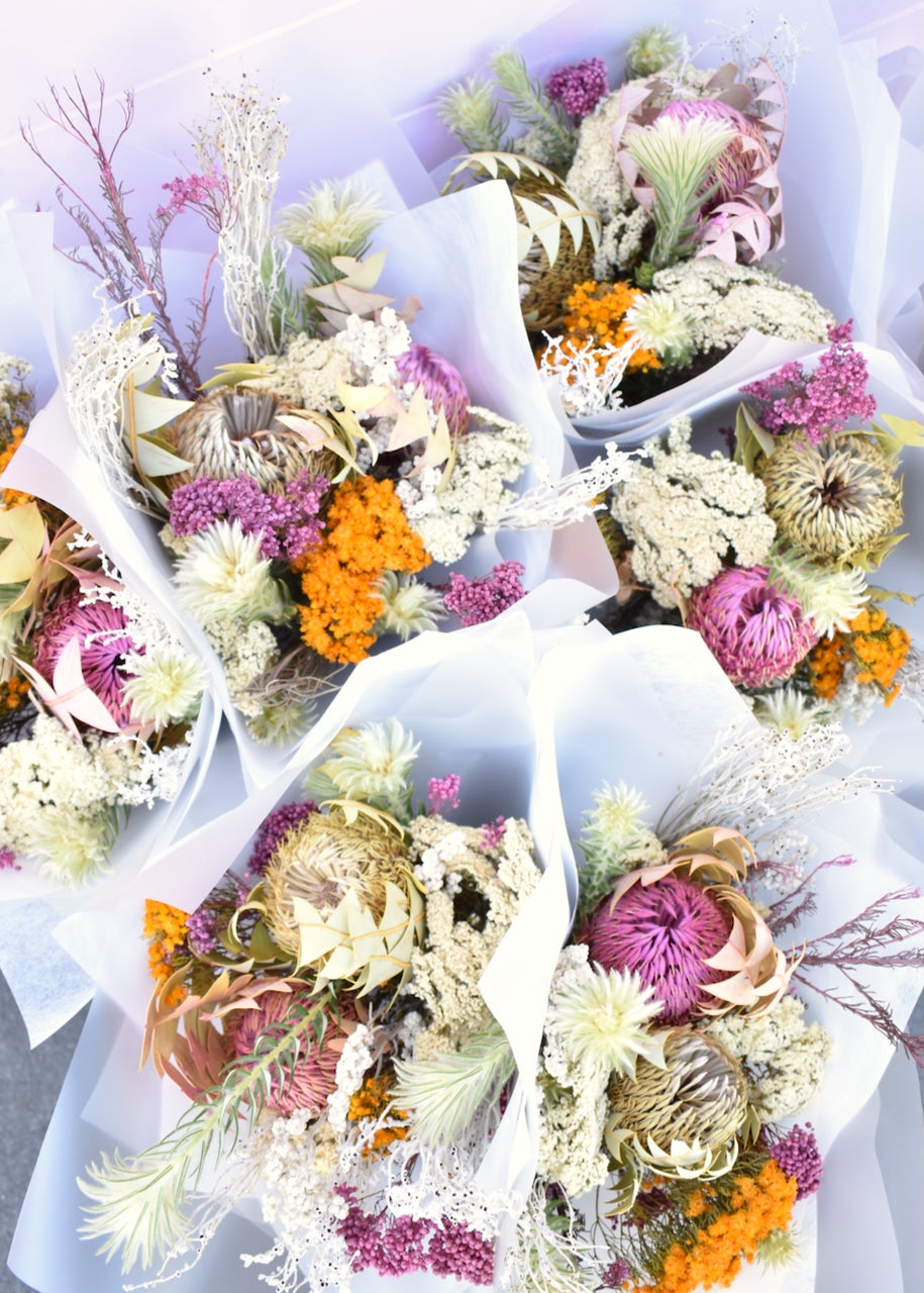 Bundles of dried flowers.  Colours of pink, white, silver and mustard. Made with erica, banksia and Australian native flowers. Wrapped in white florists paper.