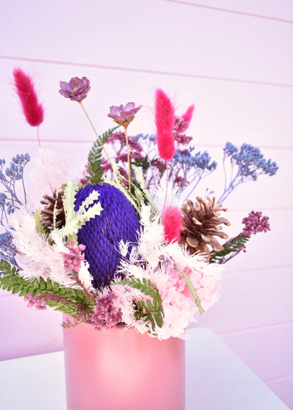 Pink pot containing dried and everlasting flowers. colours of bright purple, hot pink, white deep green and lilac. Includes bunny tails, pinecones, banksia, ming fern and more