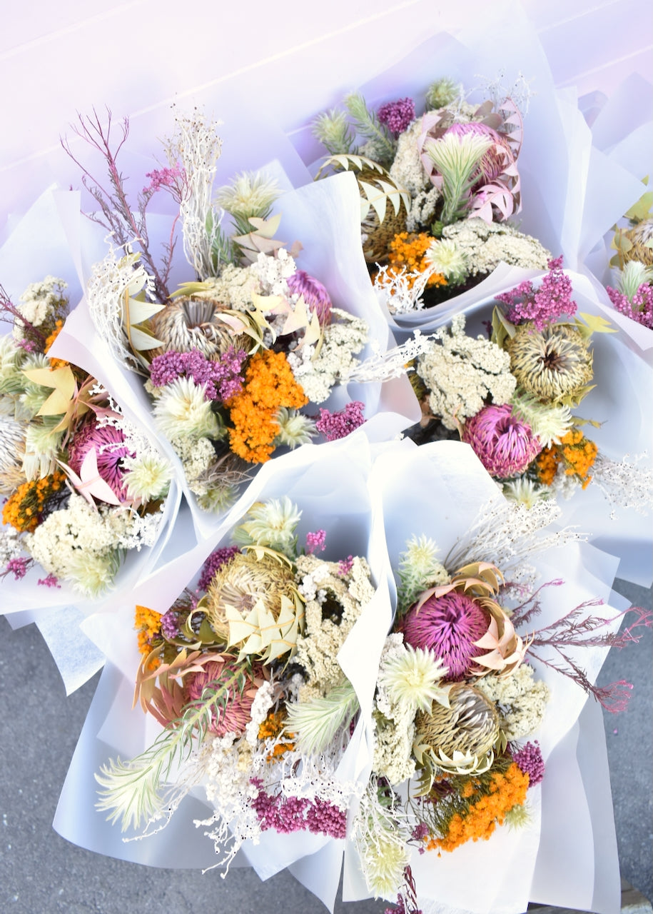 Bundles of dried flowers. Colours of pink, white, silver and mustard. Made with erica, banksia and Australian native flowers. Wrapped in white florists paper.