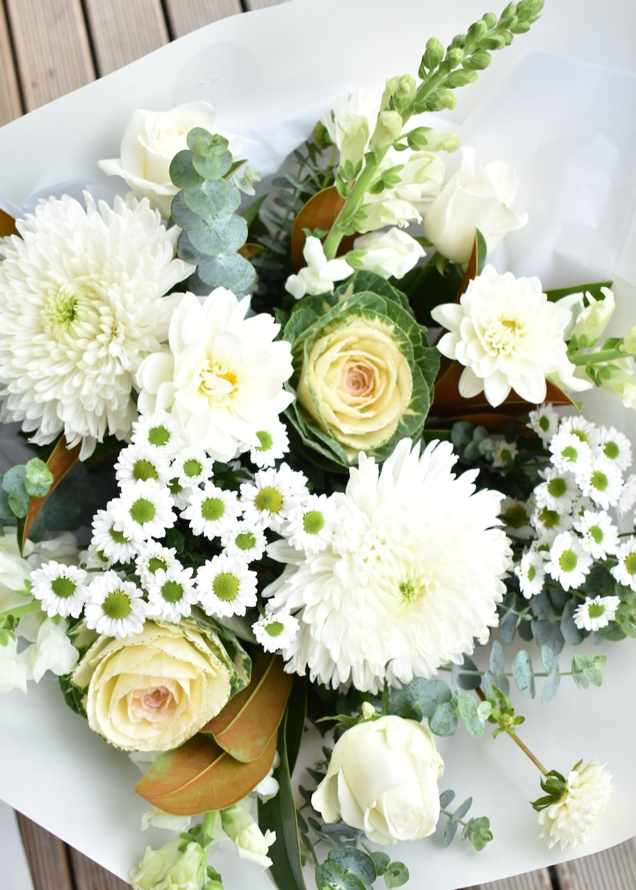 Beautiful white, cream and green fresh flower bouquet. Designed with white roses, daisies, chrysanthemums and foliage in a white paper wrap.