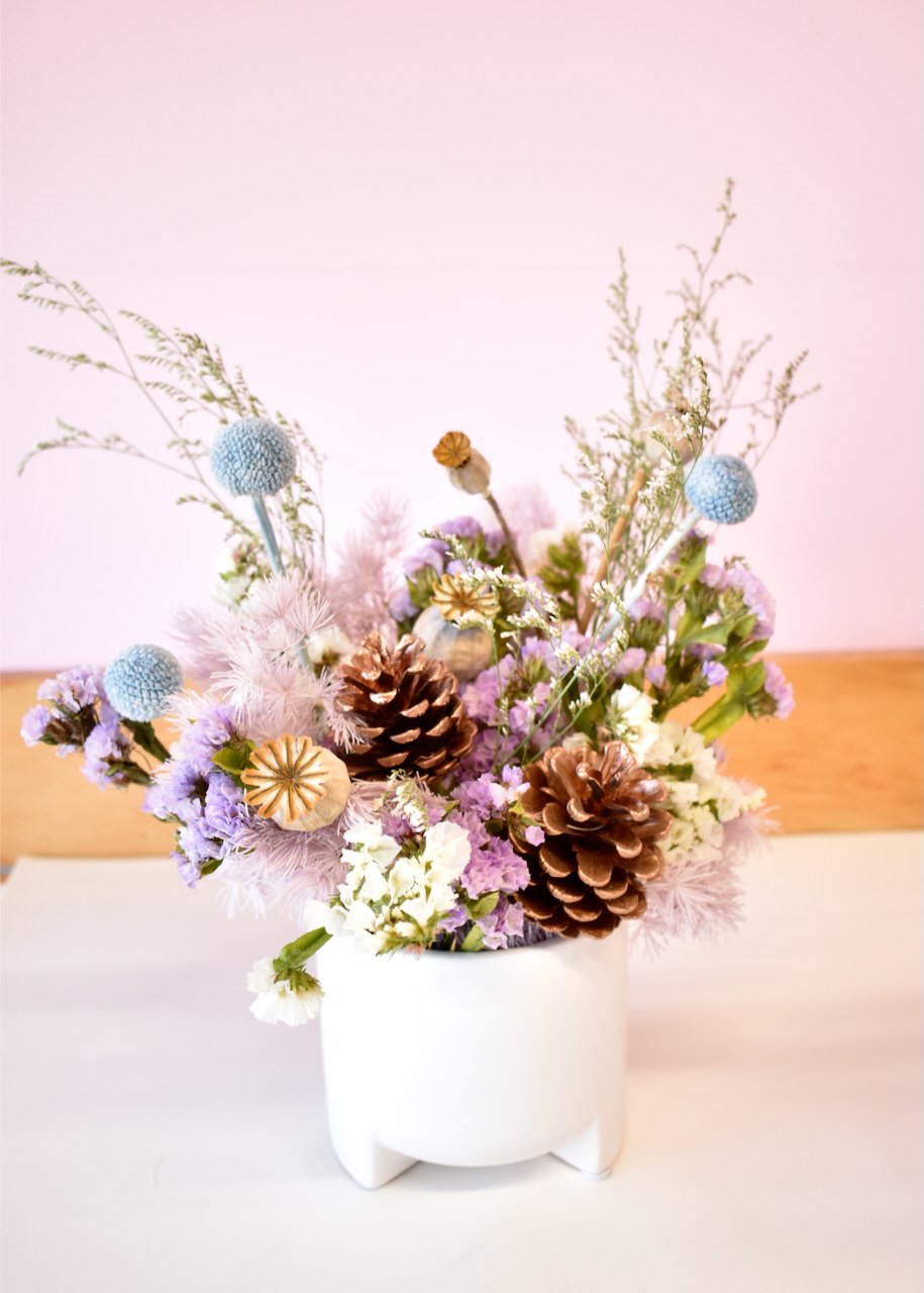 Pretty dried flower arrangement in a small white ceramic pot. Colours of pale blue, mauve and white.