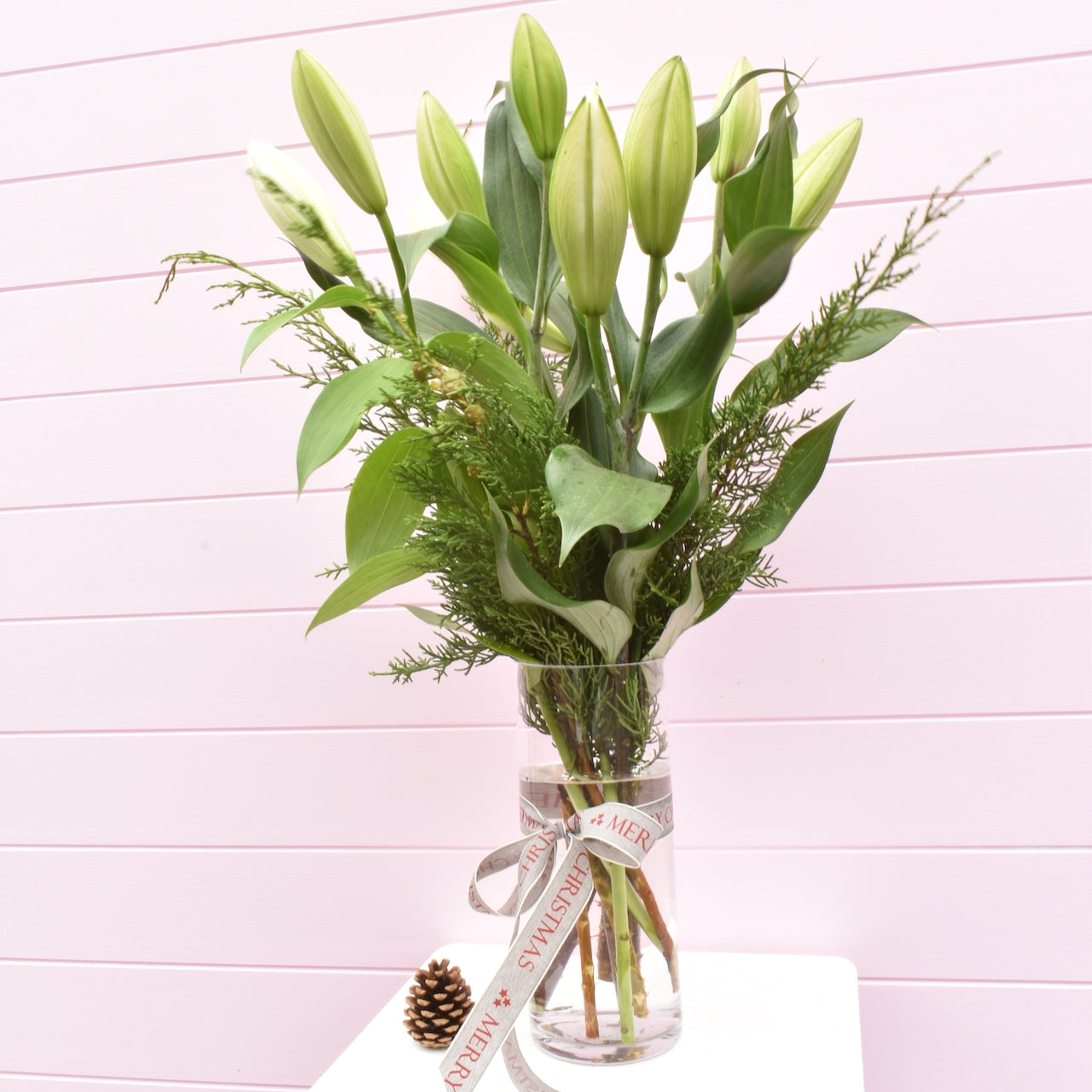 White Oriental Christmas lilies in a glass vase with Christmas foliage and Christmas ribbon