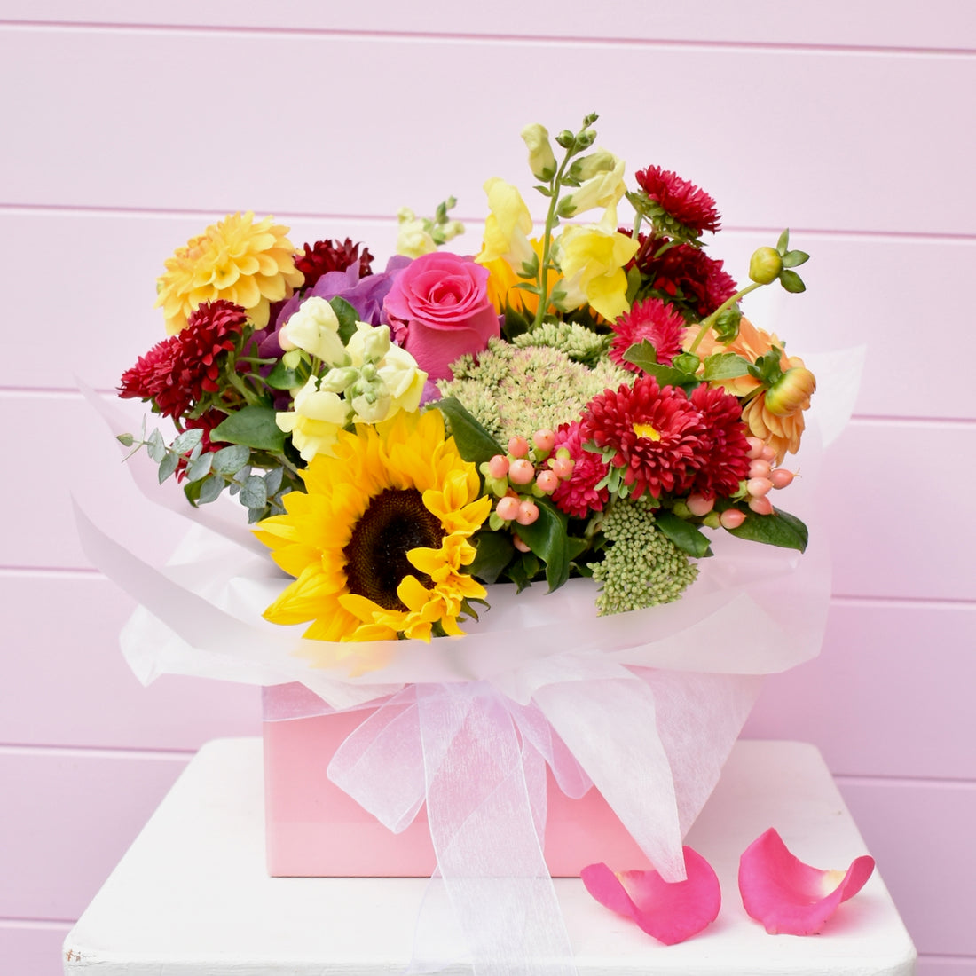 Pink box containing a colourful bouquet of flowers including sunflowers &amp; roses