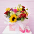 Pink box containing a colourful bouquet of flowers including sunflowers & roses