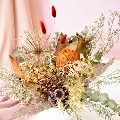 A dried flower arrangement, red bunny tails, magnolia foliage, protea, banksia, hydrangea and fern. Natural earthy colours.