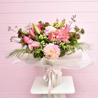 Pink flower bouquet in vase sitting on white table in front of a pink back drop