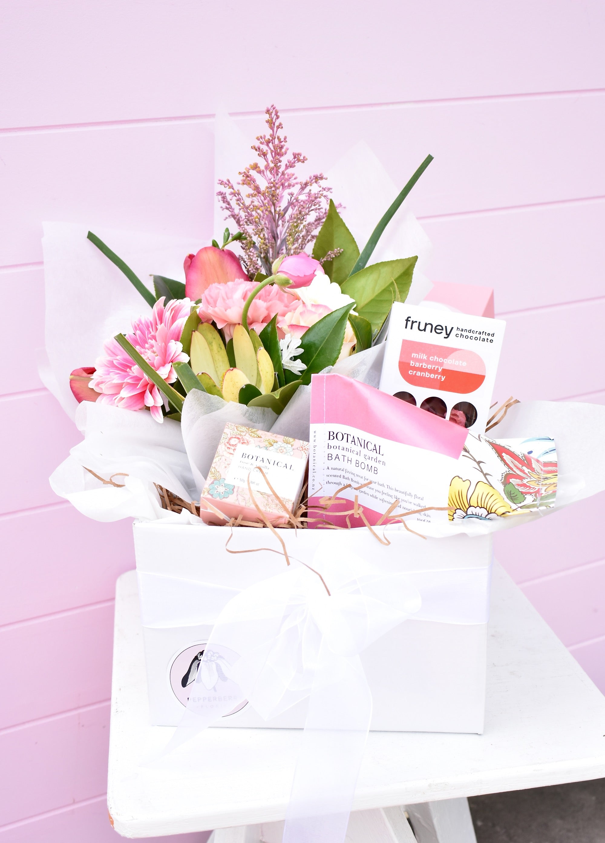Pink and white gift hamper created by a florist. Containing a bouquet of fresh flowers, hand cream, bath bomb, rose tea and chocolate bar. Presented in white box with tissue.
