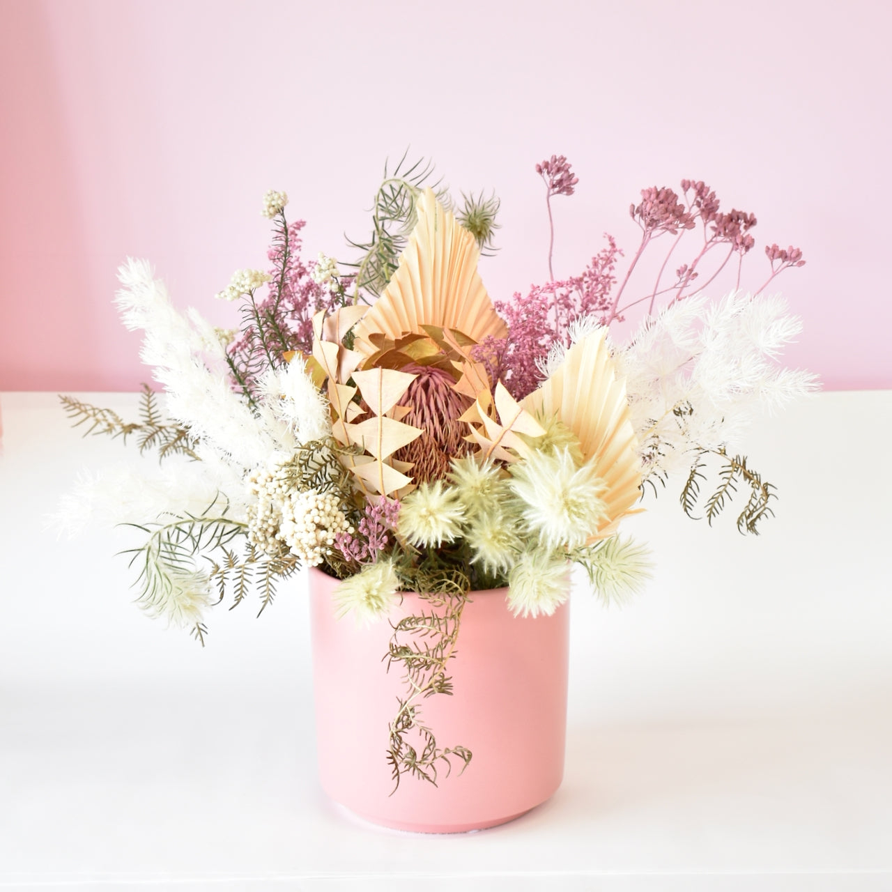 White, peach and pink dried flower bunch in a pink pot. Ferns, banksia, palm