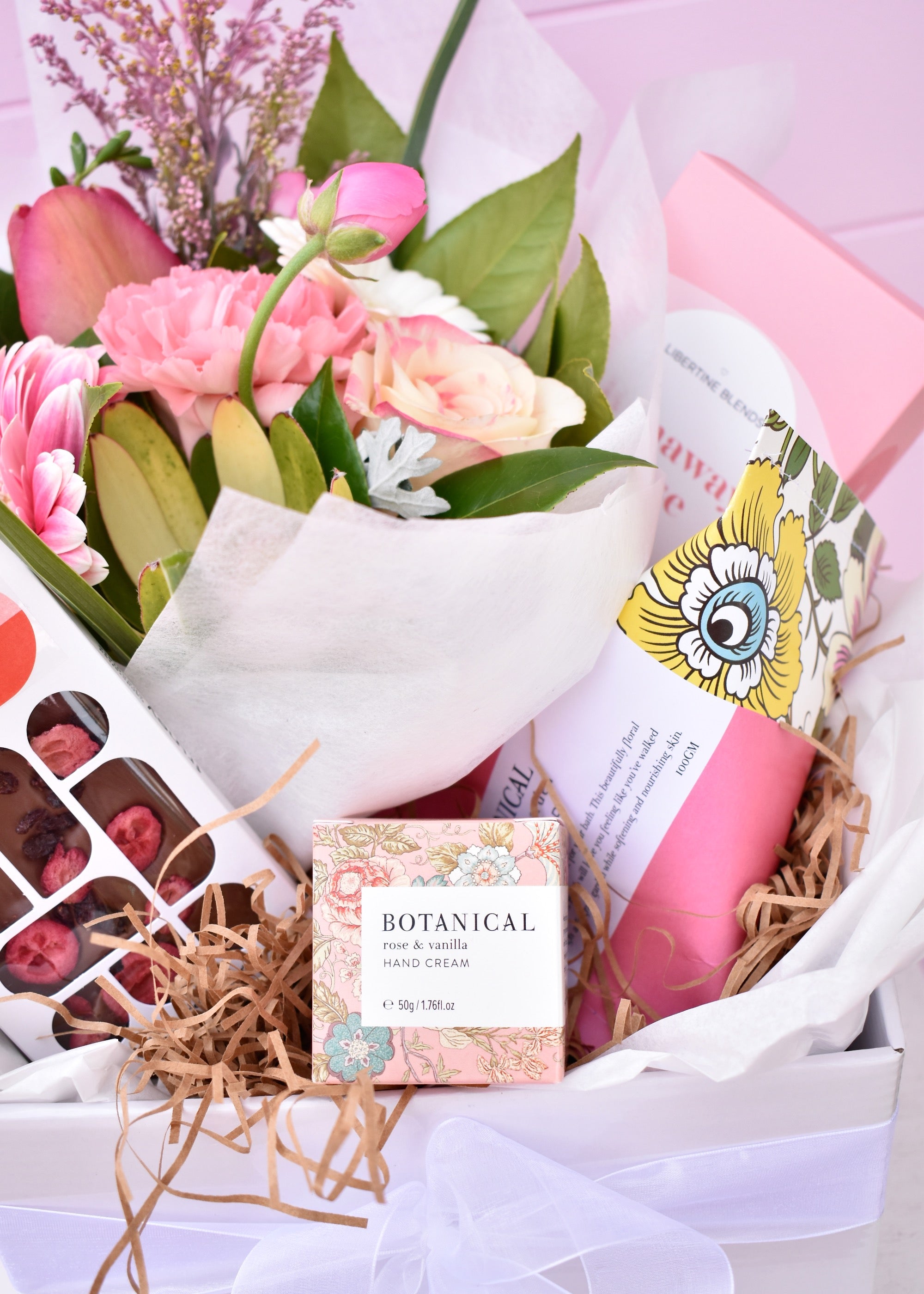 A gift box created by a florist. Fresh flower posy, box of floral hand cream, chocolate and strawberry bar, botanical bath bomb and rose tea.