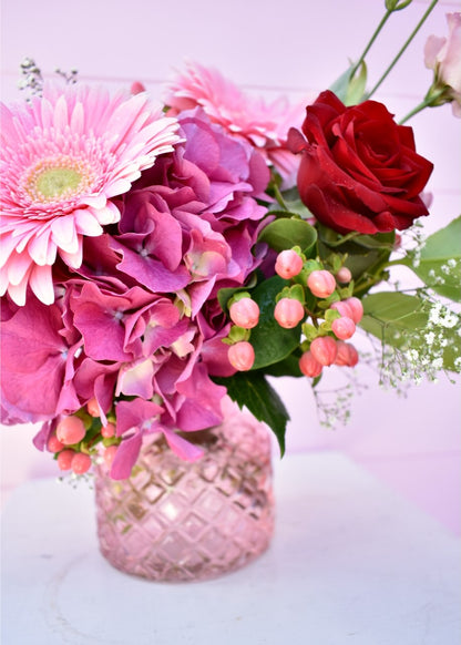Pretty pink glass vase with a bouquet of fresh flowers. Hydrangea, red roses, gerberas and berries